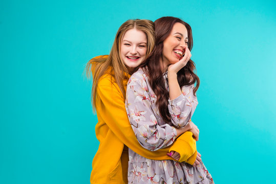 Young couple of women and girlfriends holding each other isolated over turquoise blue background