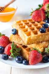 Fresh homemade food of berry Belgian waffles with honey, chocolate, strawberry, blueberry, maple syrup and cream. Healthy dessert breakfast concept with juice