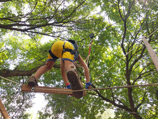 A seven-year-old boy enjoys climbing a rope park stretched high above the ground between tree...