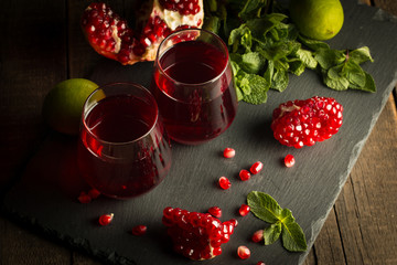Pomegranate juice with fresh pomegranate fruits on wooden background. soft drink with lime, mint and ice.