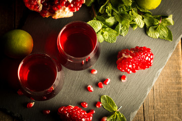 Pomegranate juice with fresh pomegranate fruits on wooden background. soft drink with lime, mint and ice.