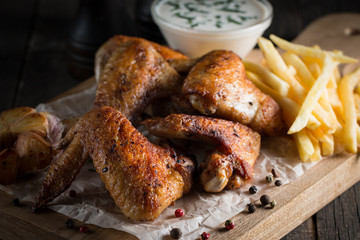 Barbecue grilled chicken wings close up with fries, tomato ketchup sauce and beer on wooden background. Meat food concept. 