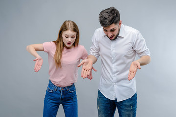 Young guy and girl pointing down isolated over gray background