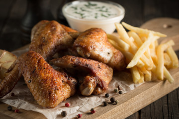 Barbecue grilled chicken wings close up with fries, tomato ketchup sauce and beer on wooden background. Meat food concept. 