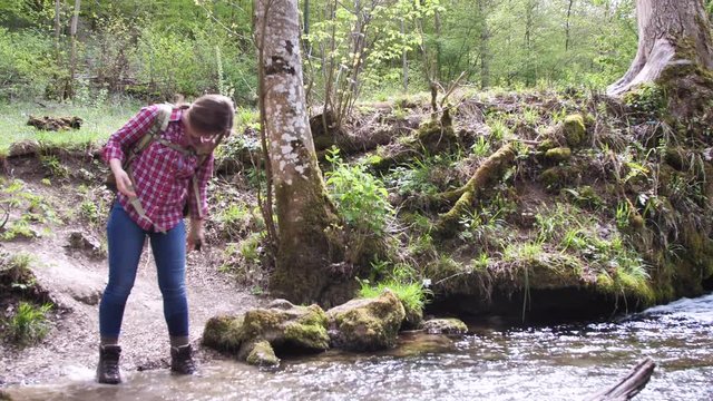 gl&uuml;ckliche junge Frau mit Rucksack beim wasser am schnellen Fluss im Wald