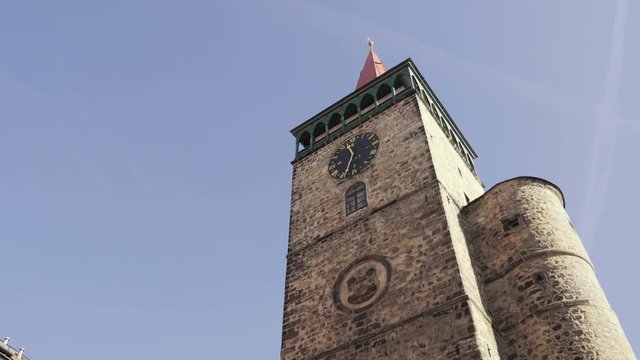 Medieval Renaissance square with stone tower and clock. View to row of houses with colorful old facades and blue sky. Age-old gas lamp and arcades. Static sunny day shot, color corrected footage