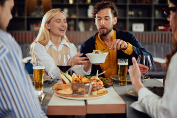 Multiethnic friends sitting at restaurant, drinking alcohol, chatting and having burgers for dinner.