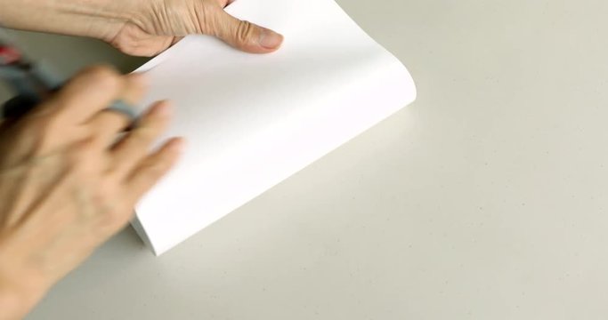 Hands cutting heart shape out of white paper sheet using scissors