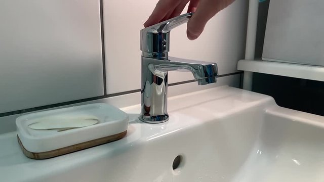 Side shot of drinkable water consumption. Ultra slowmotion of opening the water tab in bathroom with white tiles and soap in the background.
