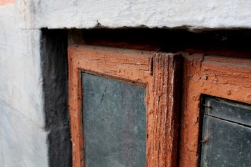 An old window in a red frame with dirty glass on a gray facade. The view is close.