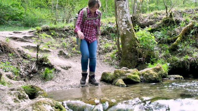gl&uuml;ckliche junge Frau mit Rucksack beim wasser am schnellen Fluss im Wald