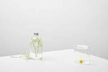 bottle with natural beauty product and white wildflowers on grey background