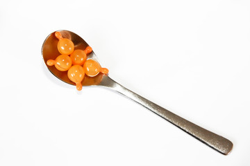 orange medicine capsules in a spoon on a white background