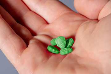 Close-up of the palm of a caucasian hand with green MDMA, Amphetamine, Army Skull, Ecstasy or XTC pills.