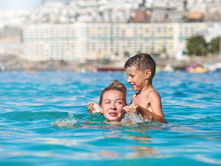 Cute European boy is splashing in the sea with his mother. They are having fun during their holidays on the seacoast.