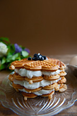 Homemade waffles with aronia, eggs and lilac flowers on the wooden table