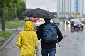 people walking under umbrella in rainy weather by city street