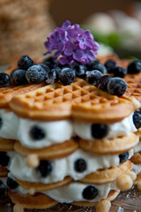 Homemade waffles with aronia, eggs and lilac flowers on the wooden table
