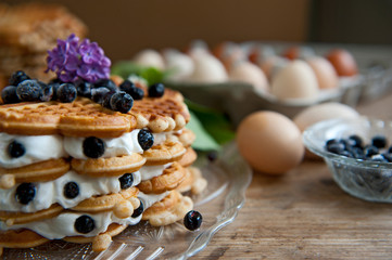 Homemade waffles with aronia, eggs and lilac flowers on the wooden table