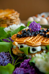 Homemade waffles with aronia, eggs and lilac flowers on the wooden table