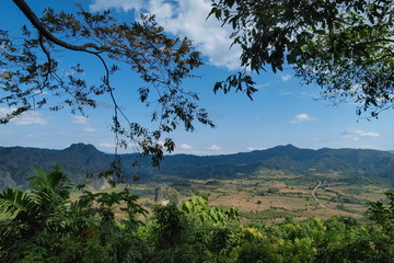 view under tree branches of long road route 1148 around with green field and mountain with blue sky background, Phu Langka View Point (photo corner), Phayao, Thailand.