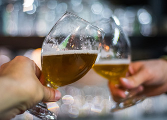 Close-up view of a two glass of beer in hand. Beer glasses clinking in bar or pub