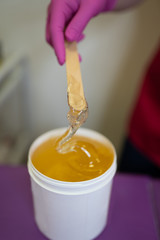The girl collects sugar paste from white cans on a wooden stick for further sugar depilation