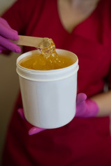 The girl collects sugar paste from white cans on a wooden stick for further sugar depilation