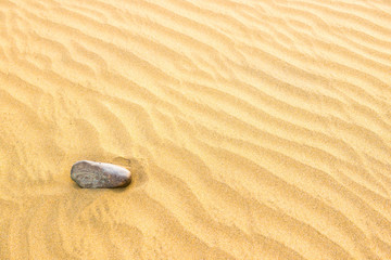 Fototapeta na wymiar Pebble lying on texture of yellow sand dunes