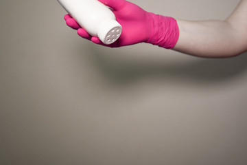 Hand in a pink glove holding a jar of talcum powder on a beige background