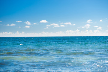 Naklejka na ściany i meble Seascape with blue water, sky and white clouds