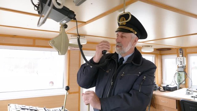 Bearded captain of ship setting radio on captain bridge. Navigation officer manage devices on navigation panel and dashboard in modern ship. Sailing and shipping concept