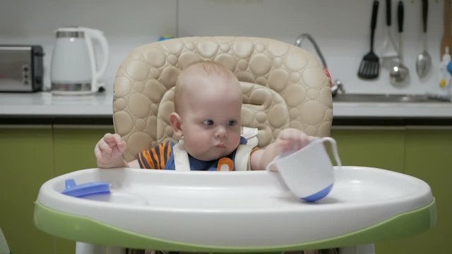 Baby sitting in a highchair and playing with a mug on a green kitchen
