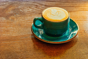 Ideal morning. Cappuccino mгg of teal color is standing on wooden tabletop of office desk. Image shot with copy space of the left side