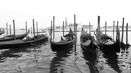 Moored or docked gondolas near the Saint Mark Square with San Giorgio di Maggiore church black and white