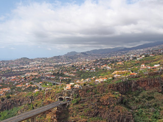 an aerial landscape view of the motorway bridge in funchal entering a tunnel in the valley with buildings and streets of the city