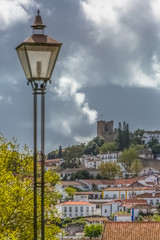 Fototapeta na wymiar View of a classic traditional lamppost, public electric light and castle and fortress of Obidos, as background