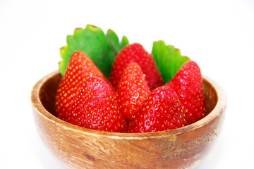 red strawberries and green leaves in a brown wooden plate on a white background