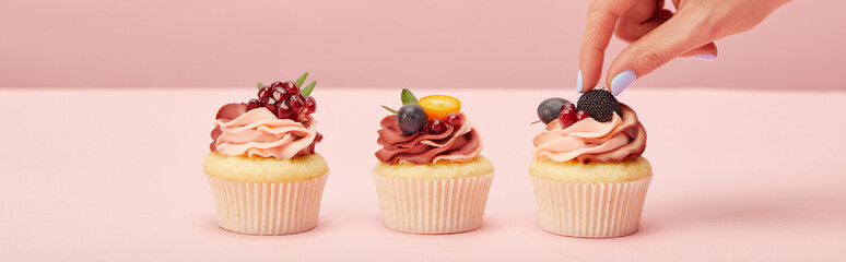 panoramic shot of woman with cupcakes on pink surface