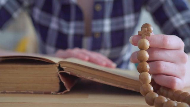 Close up of a rosary in the hands of a woman reading the Bible