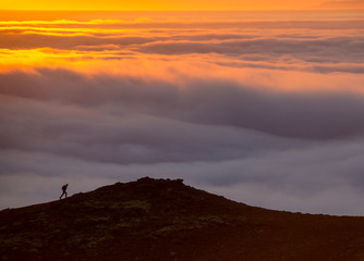 Silhouette of a man on the ridge above the sea of clouds, misty mountains at sunset in Iceland