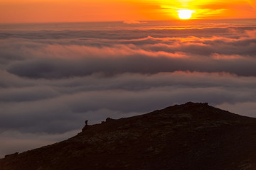 Silhouette of a man on the ridge above the sea of clouds, misty mountains at sunset in Iceland