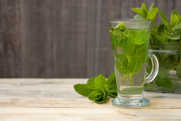 Summer fresh mint tea. Glass cup of green tea with mint leaves wooden background. Natural daylight. Copy space.
