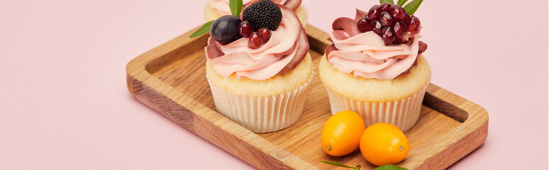 panoramic shot of cupcakes with fruits and berries on wooden tray isolated on pink
