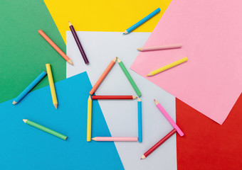 Colored pencils in the shape of a house on colored paper.