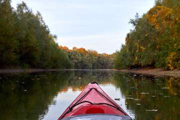 Fototapeta premium Bow of red kayak on river at calm autumn day. View on river from the bow of kayak. Autumn kayaking