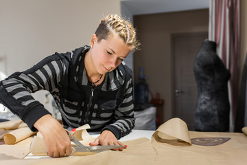 Blonde woman seamstress cuts from craft paper pattern for making clothes