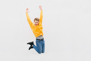 Happy guy in Casual clothes jumps against the background of a white wall, street portrait. Joyful teenager jumped to a height on a white background, isolated. Copyspace