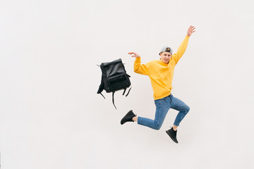 Happy young man jumping with a backpack on a white background. Stylish street boy livid with a...