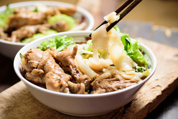 Hand holding chopsticks for eating rice noodles soup with stewed chicken wing and feet in a bowl